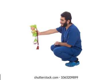 Young Doctor Sitting In Squatting Pose Giving A Green Doll To Little Kid, Isolated On A White Background.