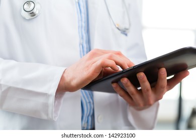 Young Doctor Standing In Clinic Reading A File Or Dossier On The Tablet Computer