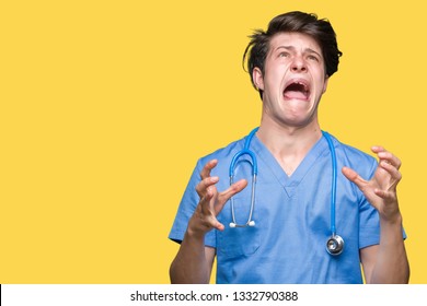 Young doctor wearing medical uniform over isolated background crazy and mad shouting and yelling with aggressive expression and arms raised. Frustration concept.