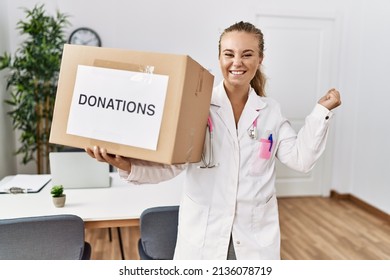 Young Doctor Woman At The Clinic Holding Donations Box Screaming Proud, Celebrating Victory And Success Very Excited With Raised Arm 