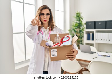 Young Doctor Woman Holding Box With Medical Items Pointing With Finger To The Camera And To You, Confident Gesture Looking Serious 