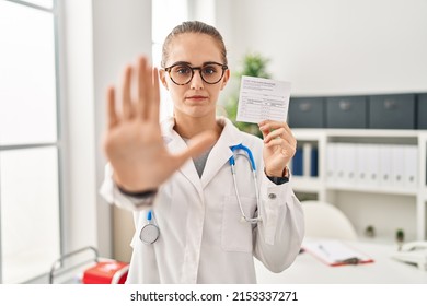 Young doctor woman holding covid certificate with open hand doing stop sign with serious and confident expression, defense gesture 