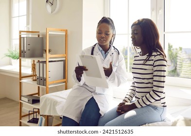 Young doctor woman holding report file with appointment and prescribe treatment to a female african american sick worried patient sitting on the couch in clinic during medical examination. - Powered by Shutterstock