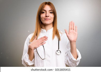 Young Doctor Woman Making An Oath On Grey Background