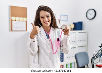 Young Doctor Woman Wearing Doctor Coat Holding Stethoscope Smiling Happy And Positive, Thumb Up Doing Excellent And Approval Sign 