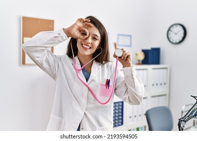 Young Doctor Woman Wearing Doctor Coat Holding Stethoscope Smiling Happy Doing Ok Sign With Hand On Eye Looking Through Fingers 