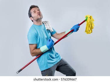 Young Domestic Service Man Or Happy Husband Cleaning Home Playing With Mop A Song On Air Guitar Having Fun Enjoying Isolated On Even Background In Housekeeping And Home Cleaning Concept