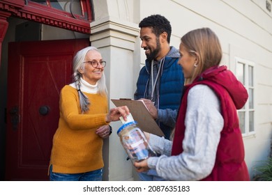 Young Door To Door Fundraisers Talking To Senior Woman And Collecting Money For Charity In Street.