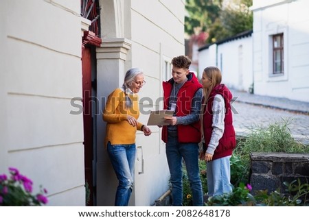 Young door to door volunteers talking to senior woman and taking survey at her front door.
