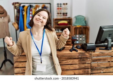 Young down syndrome woman working as manager at retail boutique very happy and excited doing winner gesture with arms raised, smiling and screaming for success. celebration concept. 