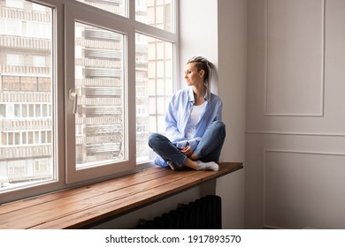 Young dreamy girl with dreadlocks sitting on a window - Shutterstock ID 1917893570