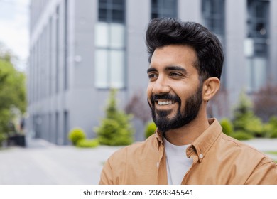 Young dreamy man close-up smiling and looking to the side, portrait of a student businessman in the air outside an office building, in casual clothes. - Powered by Shutterstock