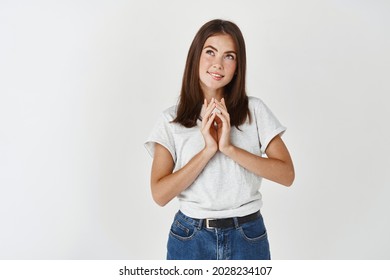 Young dreamy woman having a plan, steeple fingers and looking at upper left corner with pleased smile, imaging her idea, standing over white background