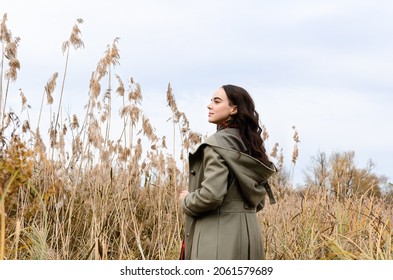 Young Dreamy Woman Wearing Grey Old Fashioned Coat Stands In The Dry Grass Reeds Field Looking Away.