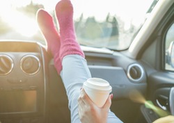 Young Drinking Coffee Take Away With Feet In Warm Socks On Car Dashboard -  Travel ,road Trip And Winter Concept - Focus On Paper Cup Hand - Warm Filter With Original Back Sun Light