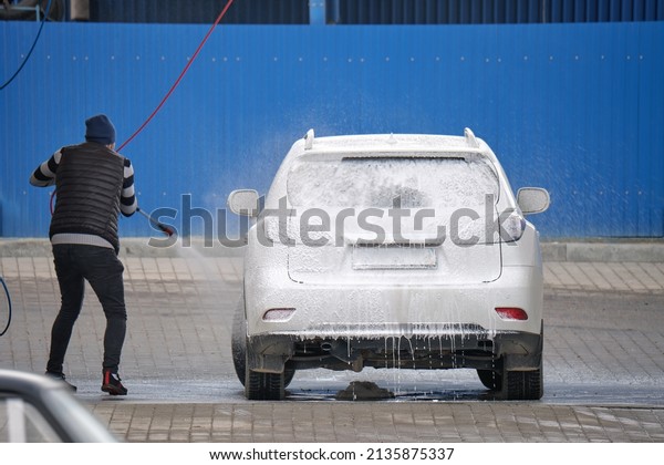 Young driver man washing his car\
with contactless high pressure water jet in self service car\
wash