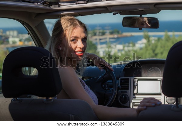 Young driver,\
pretty blonde woman behind steering wheel. Female riding using car,\
traveling, going on\
vacations.