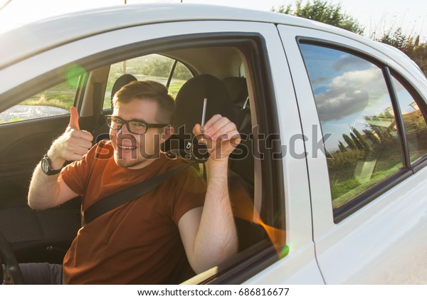 Young\
driver showing car keys and thumbs up happy. Man holding car key\
for new automobile. Rental cars or drivers licence concept with\
male driving in beautiful nature on road\
trip.