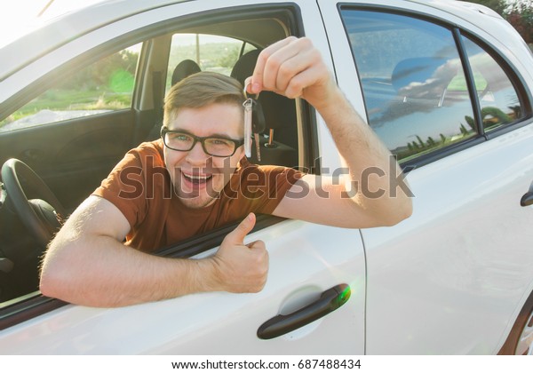 Young
driver showing car keys and thumbs up happy. Man holding car key
for new automobile. Rental cars or drivers licence concept with
male driving in beautiful nature on road
trip.