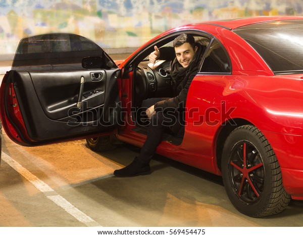 young driver sitting in sport car showing thumbs up\
with opened door