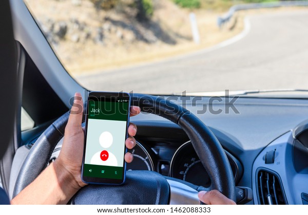 Young driver, using smartphone, on\
the road in the car. Distraction and danger on the\
road.