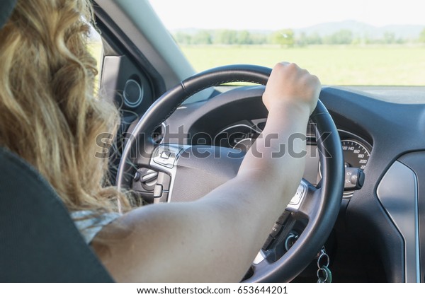 Young driver woman\
is driving a car. View from behind the seated driver. All potential\
trademarks are removed.