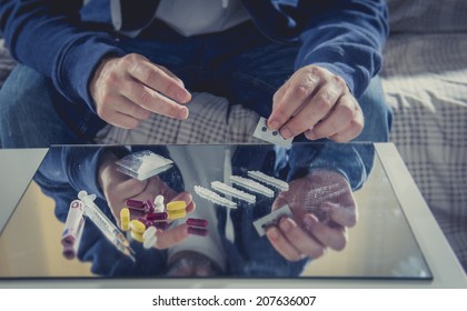 Young Drug Addict Man On Hood Sniffing Cocaine On Mirror With Rolled Banknote At Home Alone Representing The Concept Of Young People Using And Abusing Drugs