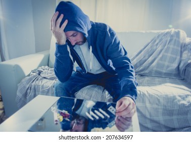 young drug addict man wearing hood preparing a shot for snorting or sniffing cocaine lines on mirror with rolled banknote at home alone representing the concept of young people using and abusing drugs
