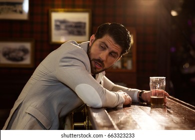 Young drunk man sitting at the counter in a pub or a bar and drinking beer