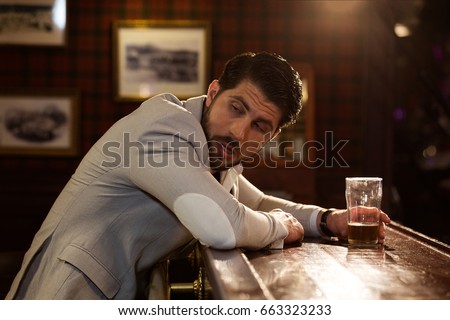 Young drunk man sitting at the counter in a pub or a bar and drinking beer