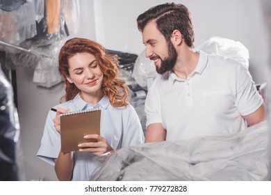 Young Dry Cleaning Workers With Jacket In Bag At Warehouse