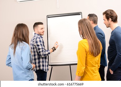 Young Dynamic Business Team Man And Woman Discussing Around A Flip Chart White Board In Meeting Room