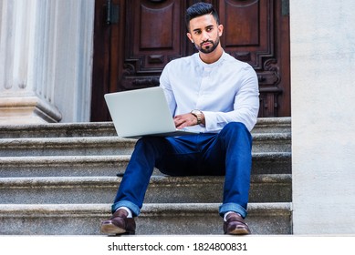 Young East Indian American College Student With Beard Studying In New York City, Wearing White Shirt, Blue Pants, Black Leather Shoes, Sitting On Stairs Outside Office, Working On Laptop Computer.
