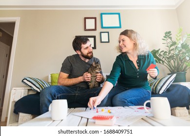 Young Eastern European Couple Playing Table Game At Home During Corona Virus Quarantine. Smiling And Looking At Each Other.