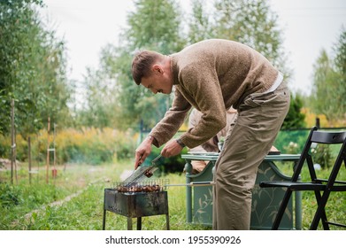 A Young Eastern European Man Prepares A Barbecue, Roasts Fragrant Meat On The Grill. Concept Of A Romantic Picnic For A Young Couple.