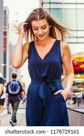 Young Eastern European Woman With Long Brawn Hair Traveling In New York City, Wearing Blue Sleeveless, V Neck, Jumpsuit, Walking On Street In Middletown Of Manhattan, Looking Down, Thinking, Smiling.