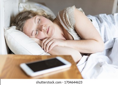 Young Eastern European woman sleeping in bed with mobile phone on the foreground.