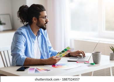 Young Eastern Freelance Graphic Designer Guy Working With Laptop And Color Swatches, Sitting At Desk In Home Office, Choosing Colour Gamma For New Design Project, Side View With Copy Space