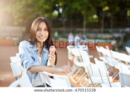 Young eastern woman eating ice cream outdoors in a city park or a concert arena waiting to start. Lifestyle concept.