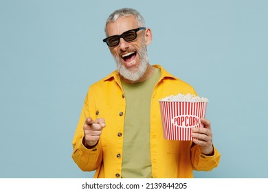 Young Elderly Happy Man In 3d Glasses Watch Movie Film Hold Bucket Of Popcorn Point Finger Camera On You Isolated On Plain Blue Background Studio Portrait. People Emotions In Cinema Lifestyle Concept