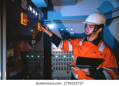 Young electrical engineer holding tablet operating main isolator switch panel, turning disconnector switch power station in control room