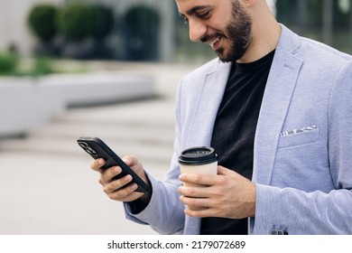 Young elegant bearded man using social media application on smartphone text messages receive news smiling outdoor. People portraits. Technology.