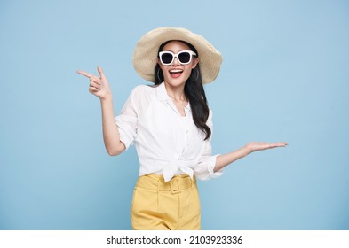 Joven y elegante mujer asiática vestida con ropa de verano sonriendo y señalando el espacio vacío de copias aislado de fondo azul.