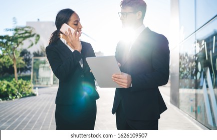 Young Elegant Black Businesswoman Having Call On Mobile Phone With Formal Male Assistant Holding Tablet Standing Near In Back Lit