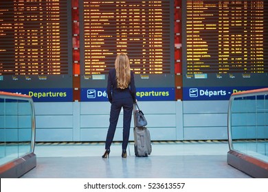 Junge elegante Geschäftsfrau mit Handgepäck im internationalen Flughafen-Terminal, Blick auf Informationsbrett, Überprüfung ihres Fluges. Flugbegleiter mit Koffer.