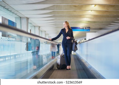Young elegant business woman with hand luggage on travelator on international airport terminal. Cabin crew member with suitcase.