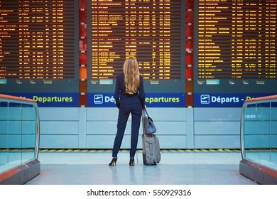 Young elegant business woman with hand luggage in international airport terminal, looking at information board, checking her flight. Cabin crew member with suitcase. - Shutterstock ID 550929316