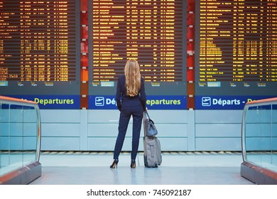 Junge elegante Geschäftsfrau mit Handgepäck im internationalen Flughafen-Terminal, Blick auf Informationsbrett, Überprüfung ihres Fluges. Kabinenbesatzungsmitglied mit Koffer