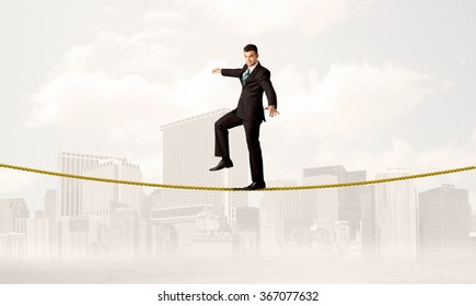 A Young Elegant Businessman Walking On Tight Golden Rope In Front Of City Buildings Landscape Background Concept