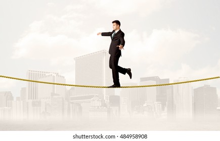 A Young Elegant Businessman Walking On Tight Golden Rope In Front Of City Buildings Landscape Background Concept